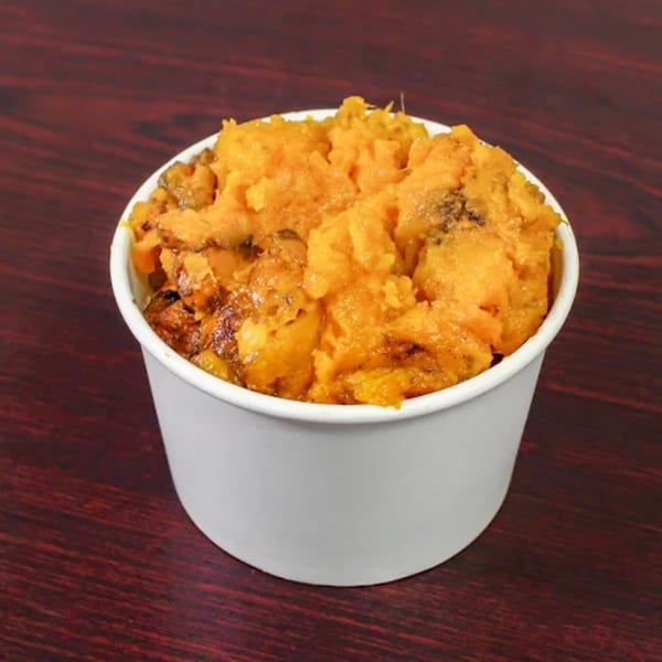 A white cup filled with American Fish & Chicken's bright orange sweet potato casserole on a wooden table.