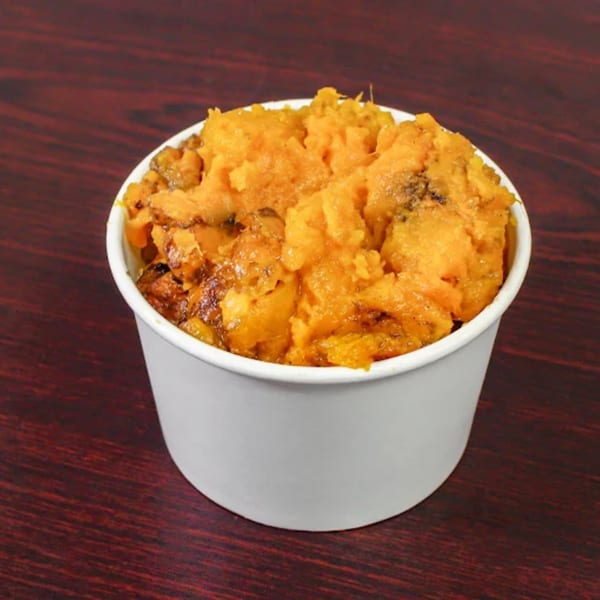 A white cup filled with American Fish & Chicken's sweet potato casserole on a dark wooden table.