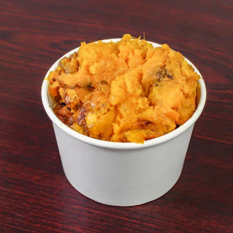 A white cup filled with American Fish & Chicken's sweet potato casserole on a dark wooden table.