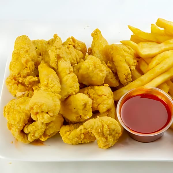 A white plate holds golden-brown fried chicken pieces, french fries, and a small cup of red sauce.