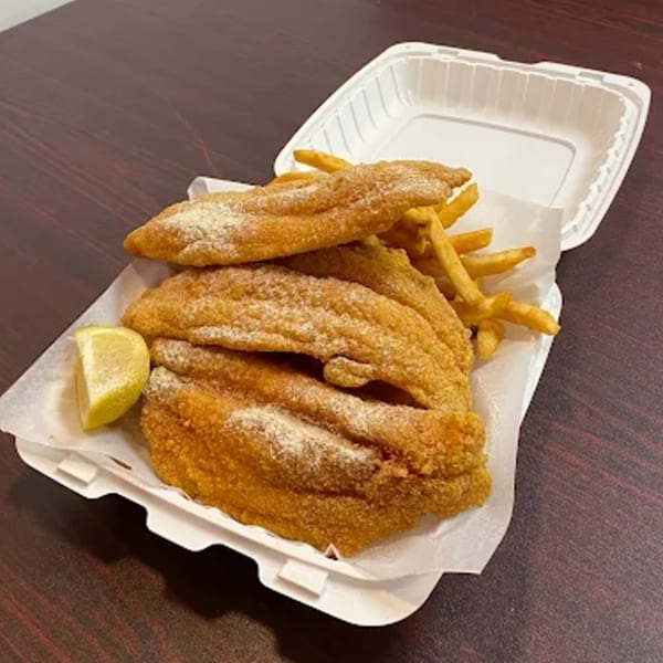 Crispy fried fish fillets with french fries and a lemon wedge in a white takeout container.