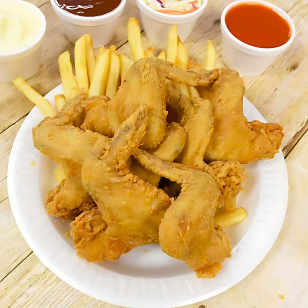 Crispy fried chicken wings and golden french fries on a white plate with various dipping sauces.