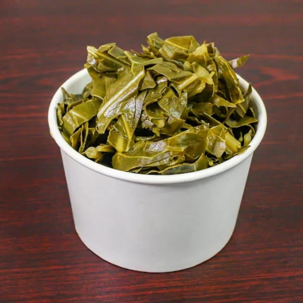 A white paper cup filled with cooked collard greens, a side dish from American Fish & Chicken.