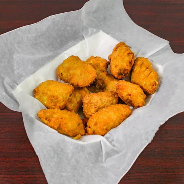 A basket of golden-brown fried okra, lined with white parchment paper, on a dark wooden surface.
