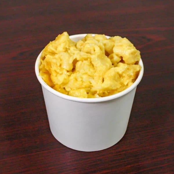 A white cup filled with creamy, golden mac and cheese on a dark wooden surface.