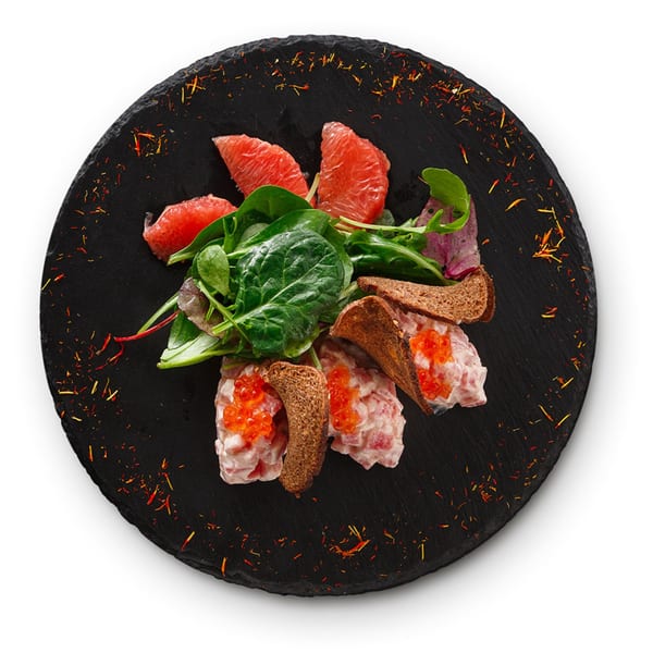 Gourmet appetizer with salmon tartare, red caviar, grapefruit, and greens on a dark slate.