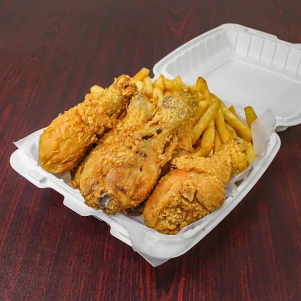 Crispy fried chicken pieces and golden french fries in a white takeout container on a dark wood table.