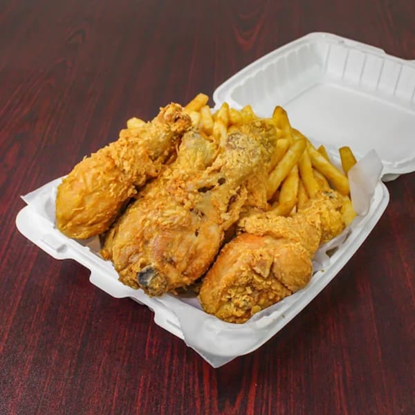 Crispy fried chicken pieces and golden french fries in a white takeout container on a wooden table.