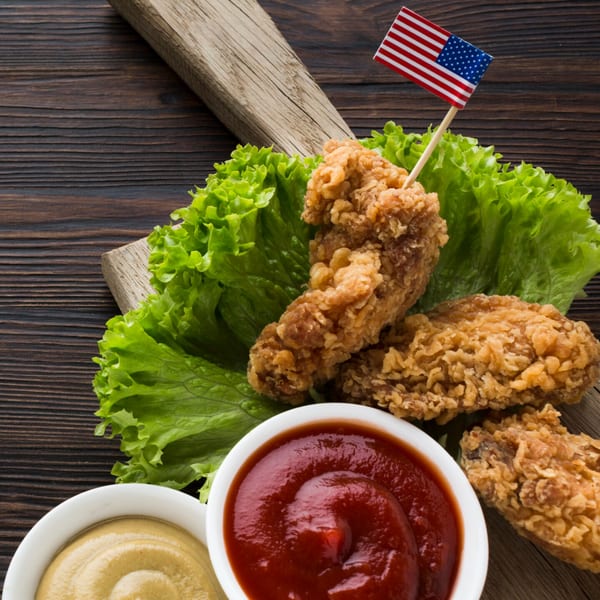 Crispy fried chicken pieces on lettuce with ketchup, mustard, and an American flag pick.